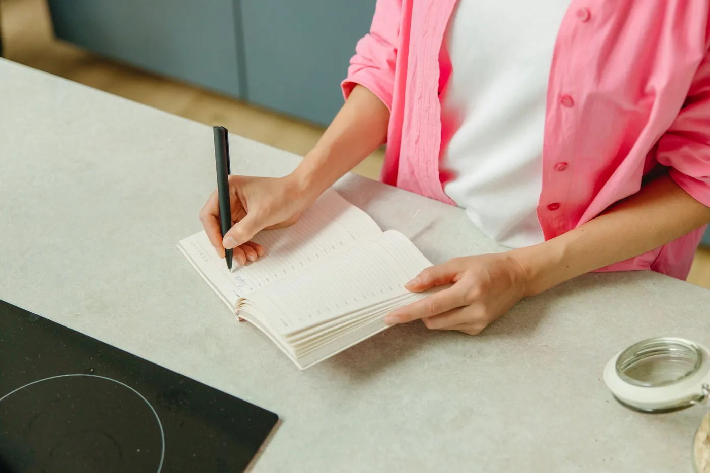 Eine Frau notiert am Küchentisch Fragen in ein Notizbuch
